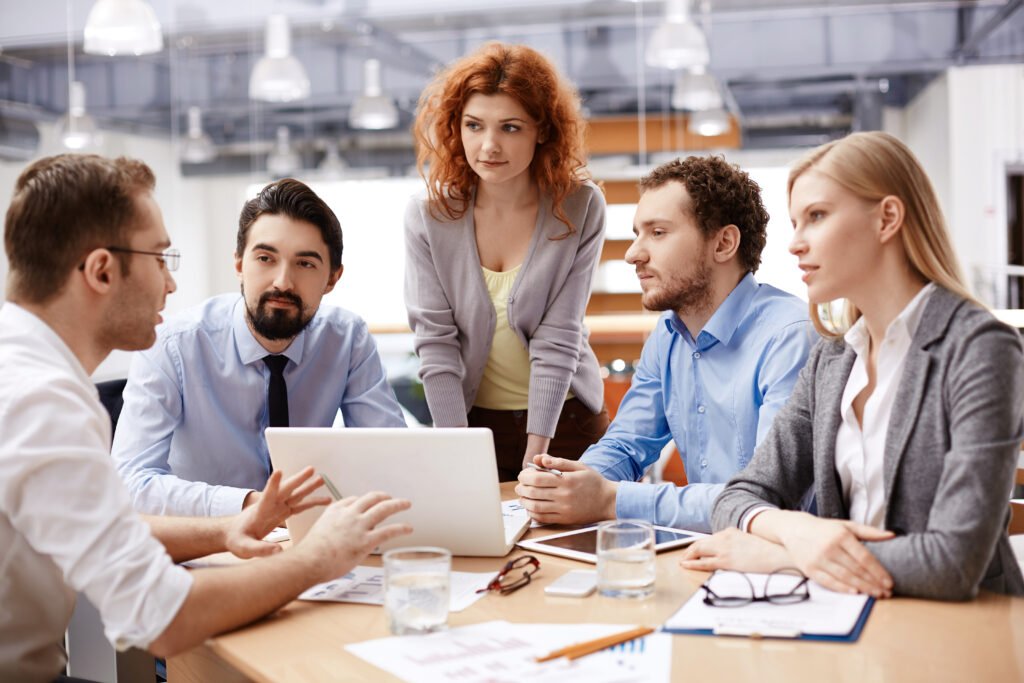 a Group of Five People in Business Attire Are Having an Efficient Discussion Around a Table with a Laptop, Papers, and Glasses of Water.