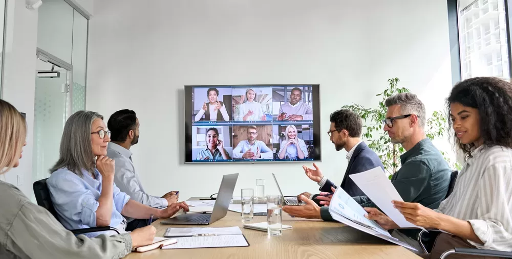 a Group of Thriving Professionals in a Meeting Room Engaging with Colleagues Through a Video Conference Call on a Large Screen. Remote Teams