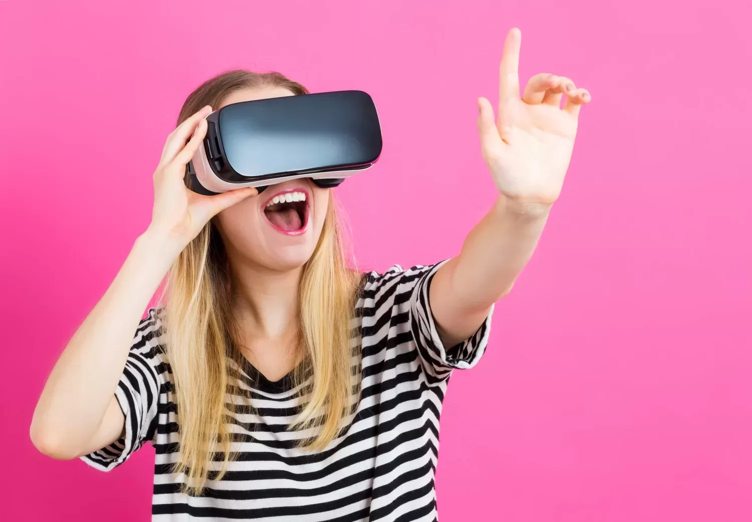 A woman wearing an AR headset excitedly gestures with her hand against a bright pink background. VR and AR