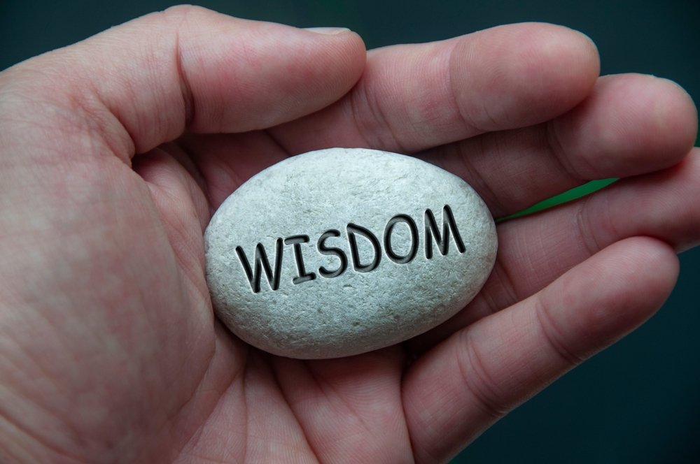 A hand holds a stone with "WISDOM" engraved on it, symbolizing the wealth of knowledge gained through a full life.