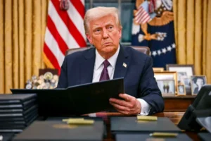 a Man Sits at a Desk in an Ornate Office, Holding a Folder, with Flags and Framed Photos in the Background, Symbolizing a New Era of Government-linked Businesses.