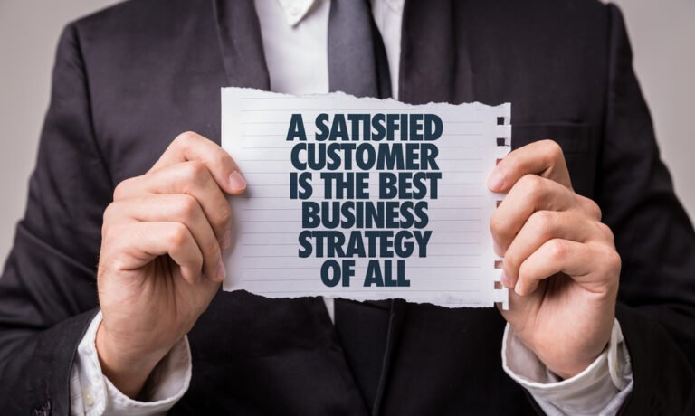 A person in a suit holds a piece of paper with the words, "A satisfied customer is the best business strategy of all," emphasizing how meeting client expectations can provide simple solutions that enhance IT management strategies.