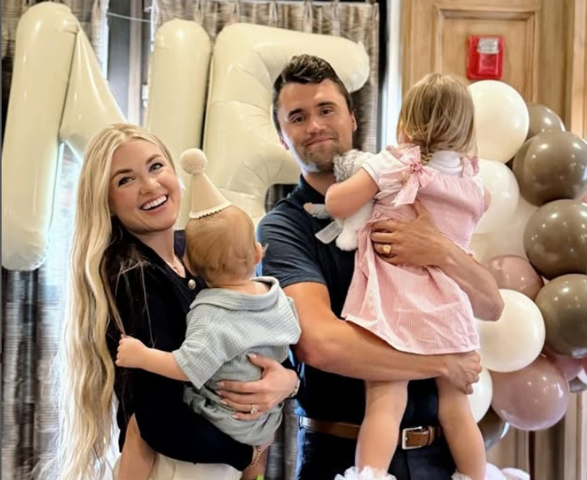A smiling man and woman hold two young children in front of large white balloons and pastel balloon decorations indoors, capturing a joyful moment in America.